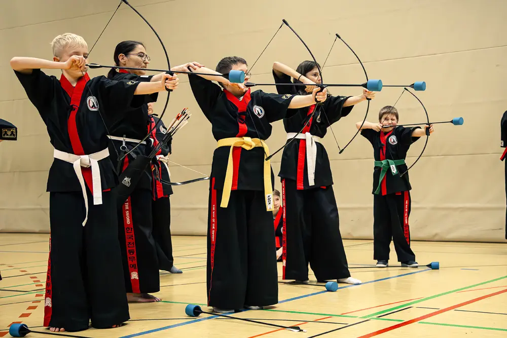 Eine Gruppe von fünf Personen in schwarzer und roter Sportkleidung übt Kummooyeh, eine koreanische Bogenschießkunst.