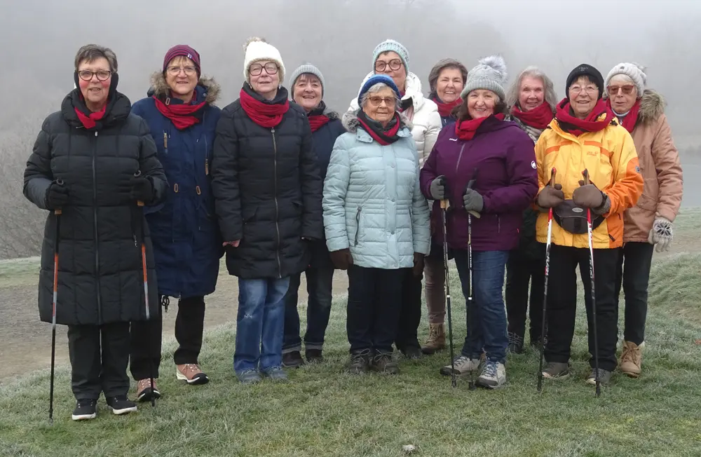 Eine Gruppe von Frauen, die in warmer Kleidung und mit Wanderstöcken ausgestattet sind, posiert auf einer grünen Wiese. Sie nehmen an einem Walking-Treff des VfR Simmern teil, um gemeinsam aktiv zu sein.