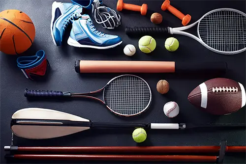 Eine Anordnung verschiedener Sportgeräte, darunter Basketball, Tennisschläger, Hanteln, verschiedene Bälle (Tennis, Fußball, Baseball, Basketball) und Ruderblätter, auf einem dunklen Hintergrund. Das Bild ist KI generiert.